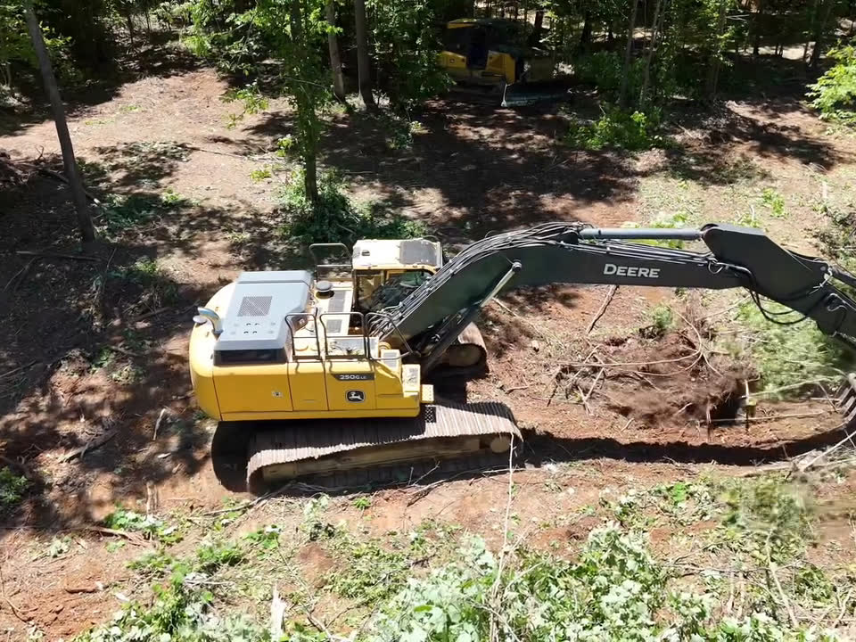 An excavator digging out roots and brush in the middle of a clearing.