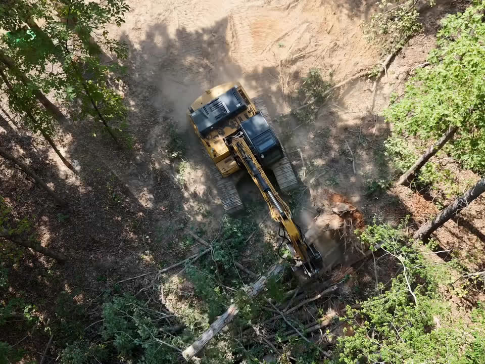 Looking straight down on an excavator pushing over trees on a wooded lot.