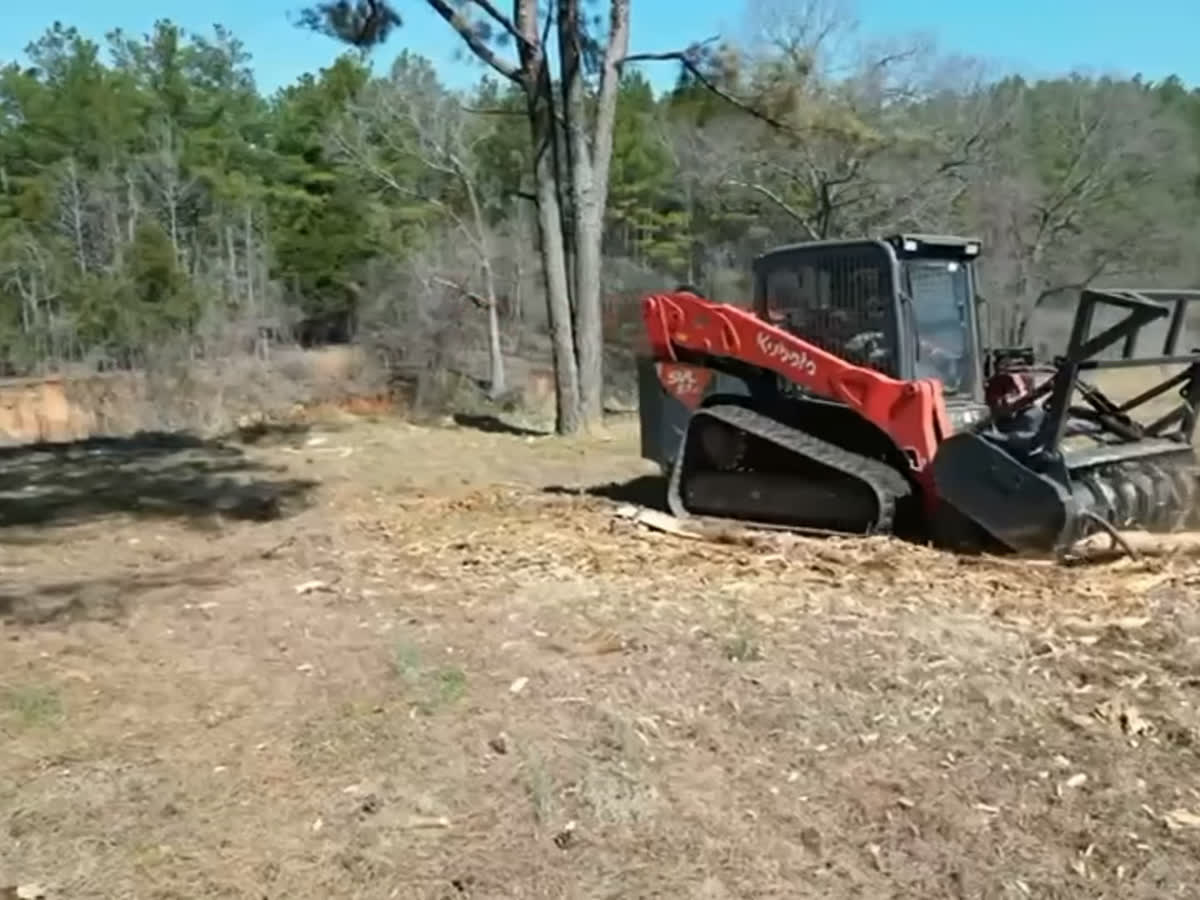 A tracked mulcher grinding brush into mulch across an open field.